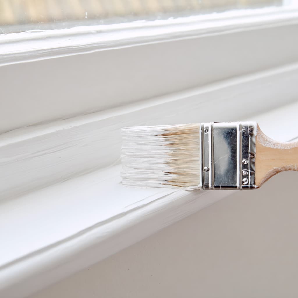 Paintbrush applying fresh white paint to window trim before property sale Paintbrush applying fresh white paint to window trim before property sale