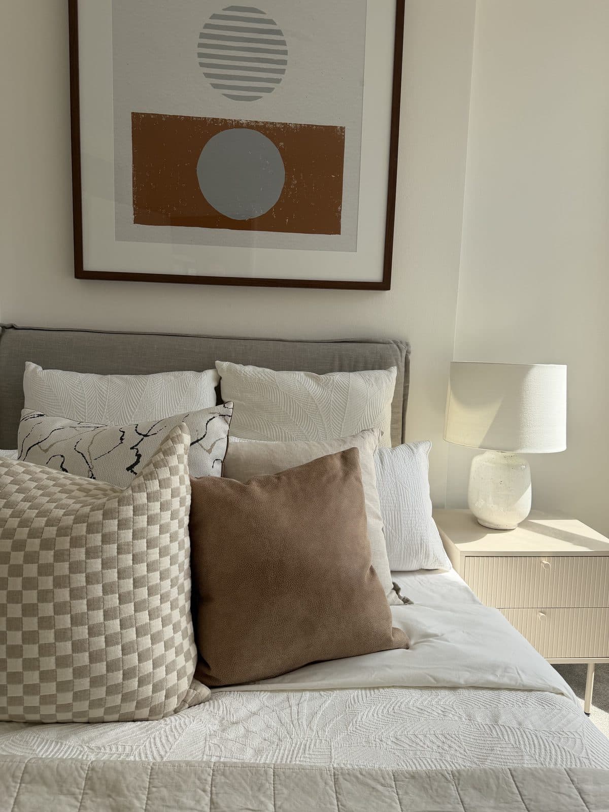 Bedroom styled with textured cushions, abstract artwork and ceramic bedside lamp — apartment styling Sydney
