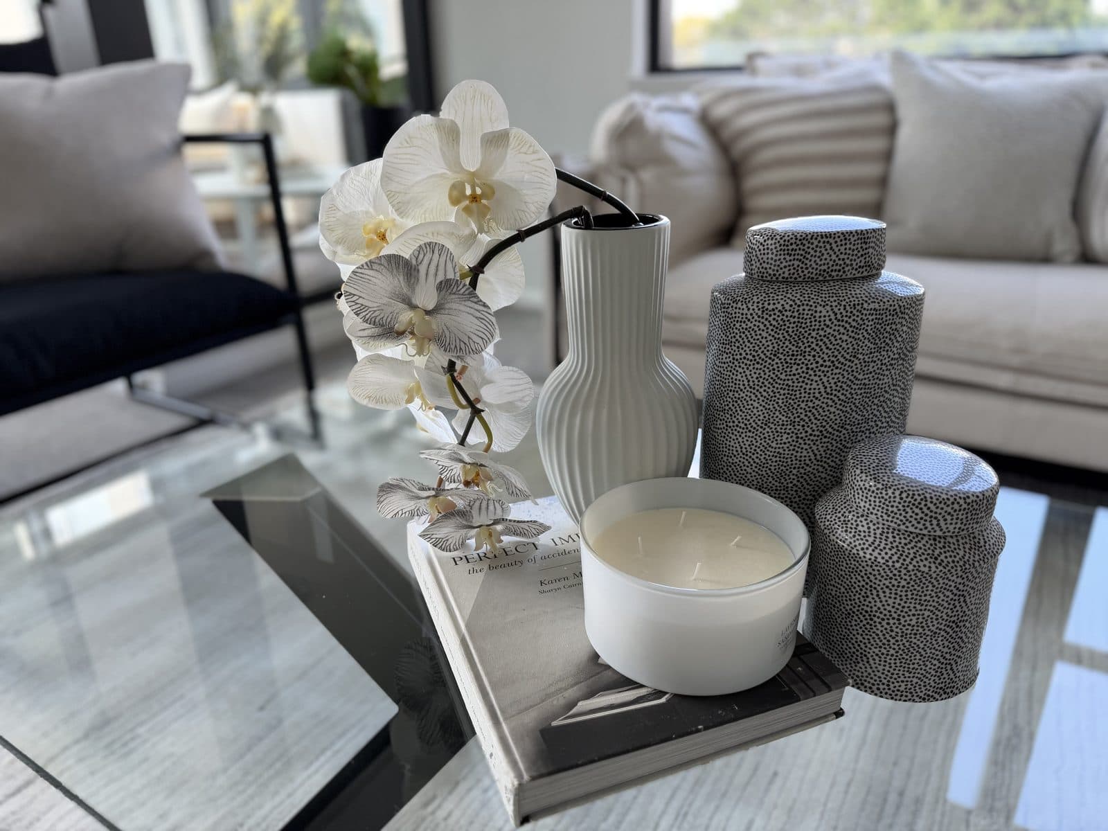 Glass coffee table styled with white orchid, ribbed vase and speckled ceramic jars — apartment styling Sydney