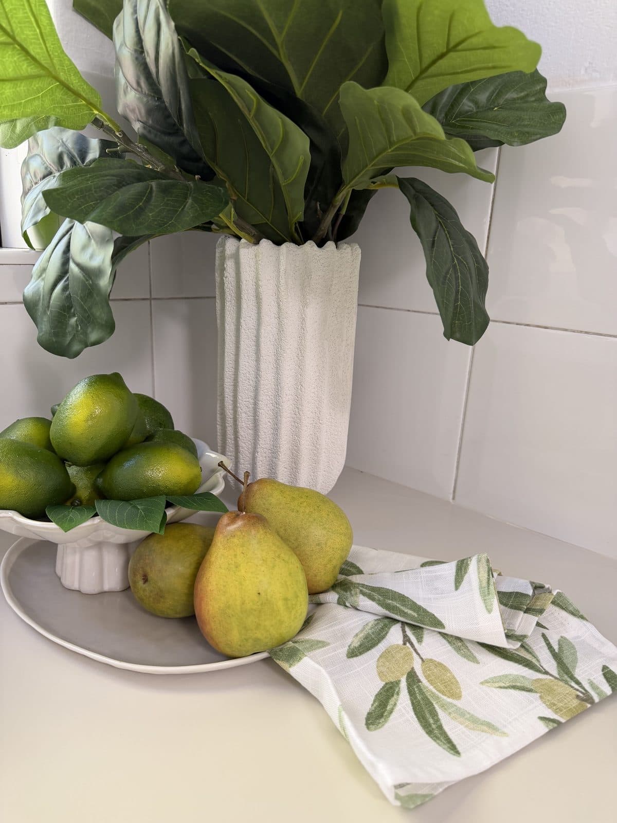 Kitchen bench styled with pears, limes and fiddle leaf fig in a ribbed white vase — apartment styling Sydney